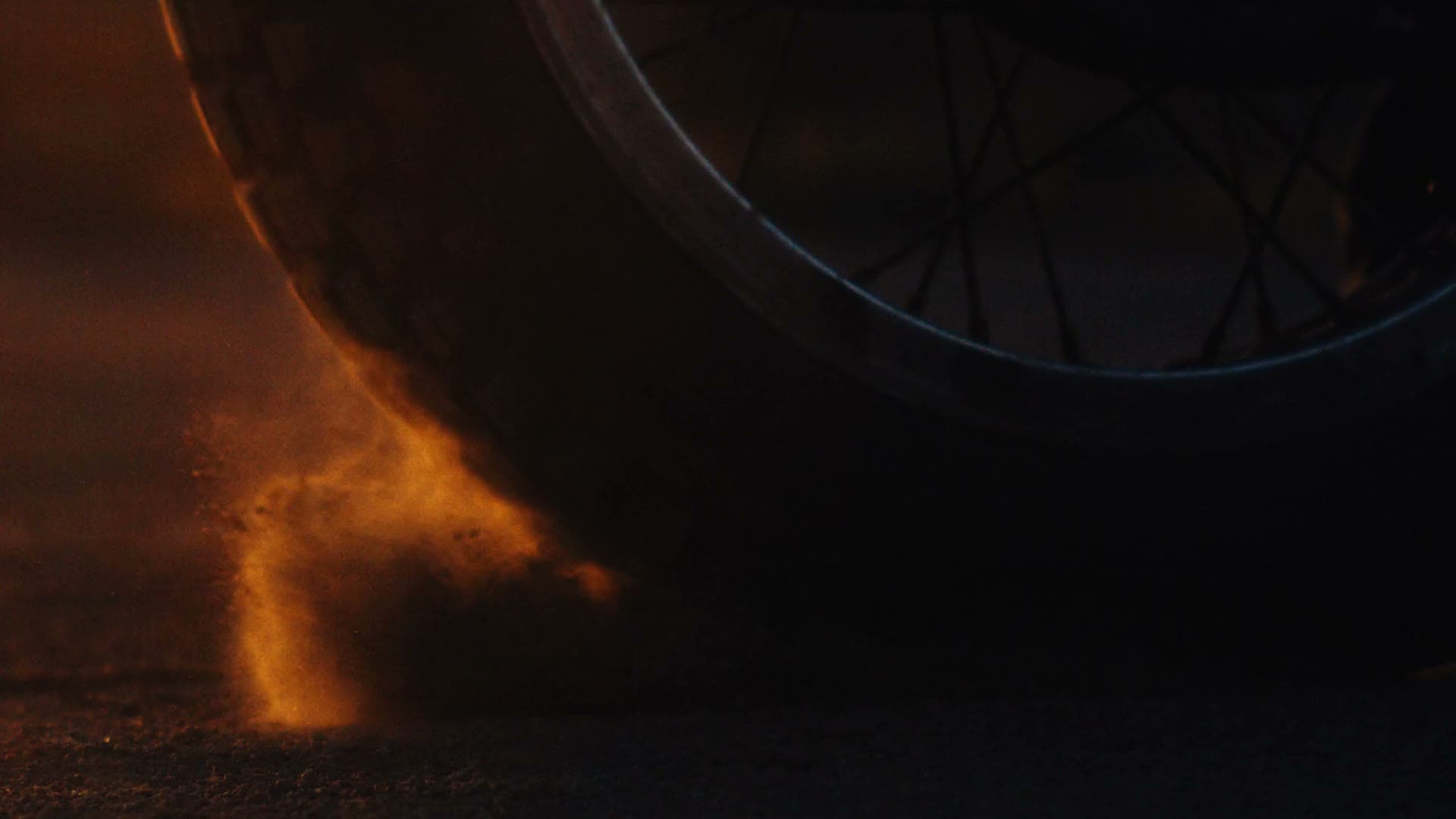 Hamilton film still, a motorcycle wheel throwing up dust in warm low light
